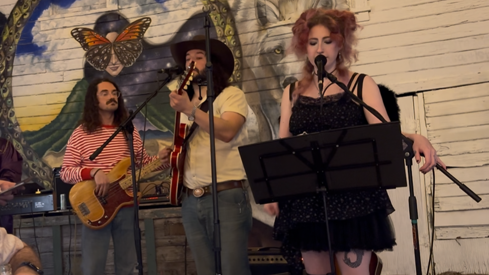 Rachel Silvers singing with a bassist and guitarist against a mural backdrop